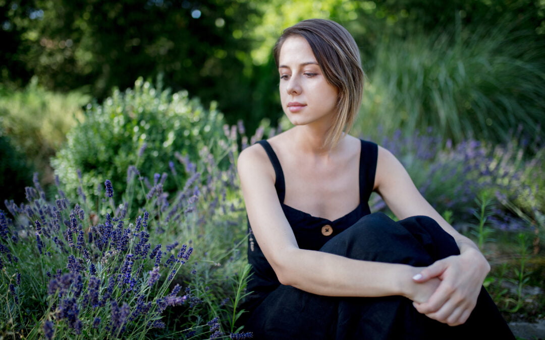 Young woman in dark dress sitting near lavender flowers